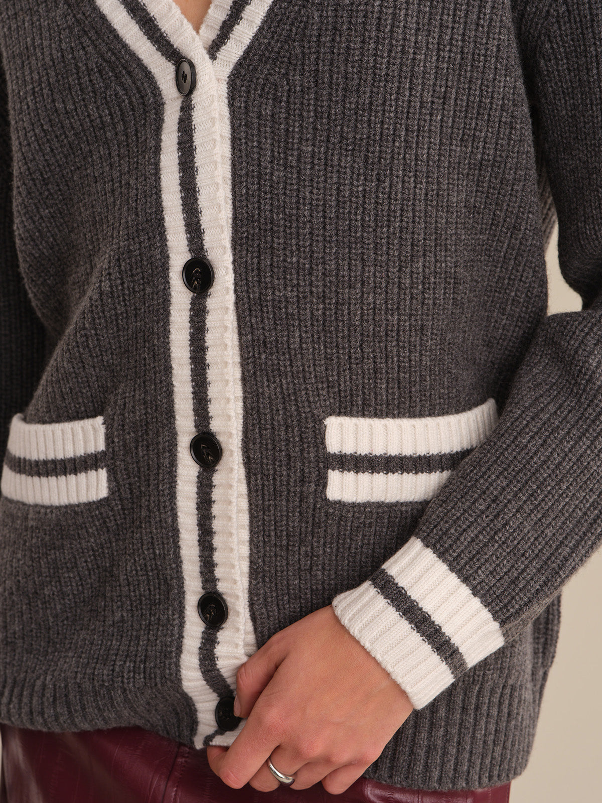 Close-up of a gray cardigan with white accents and buttons on a neutral background