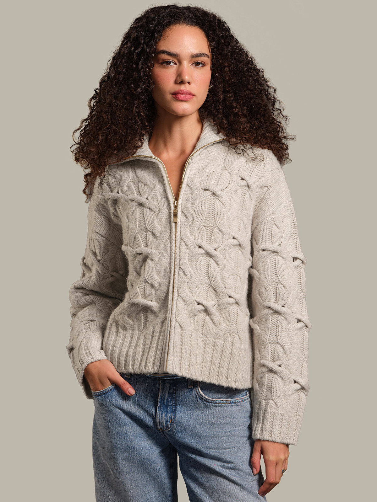 Woman wearing a beige cable knit cardigan against a neutral background