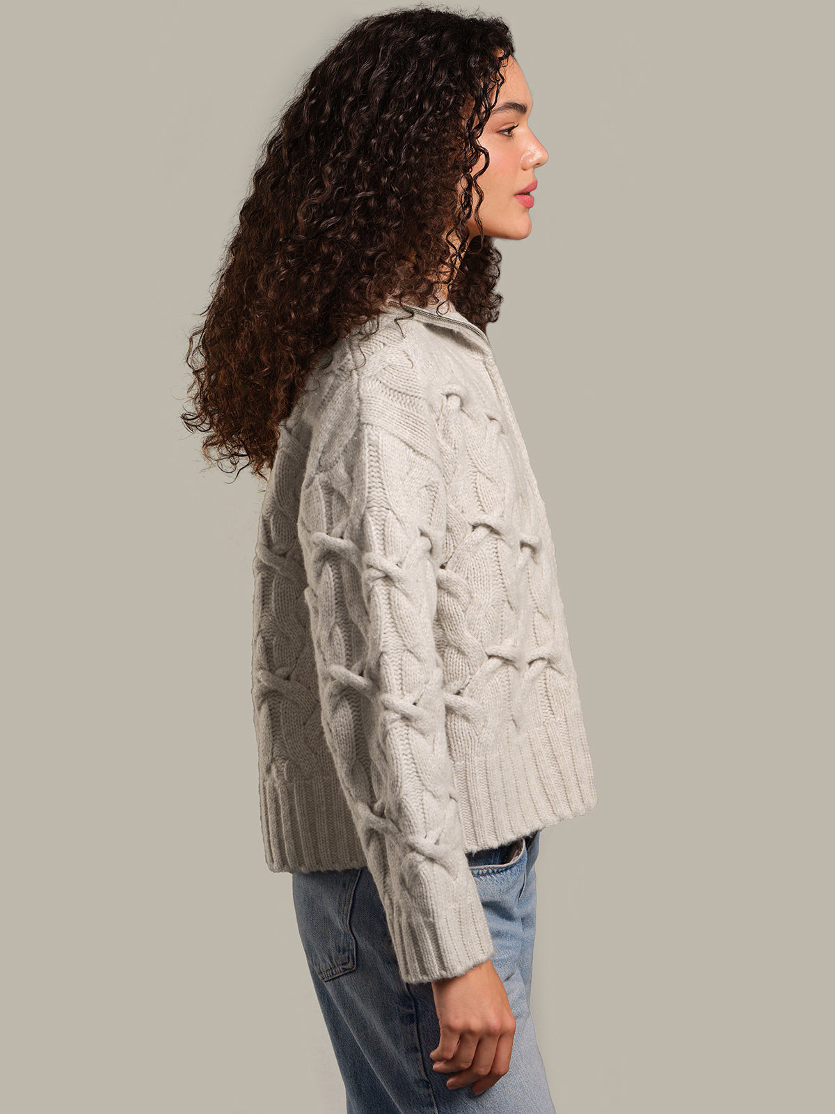 Woman wearing a light gray cable knit cardigan against a plain background