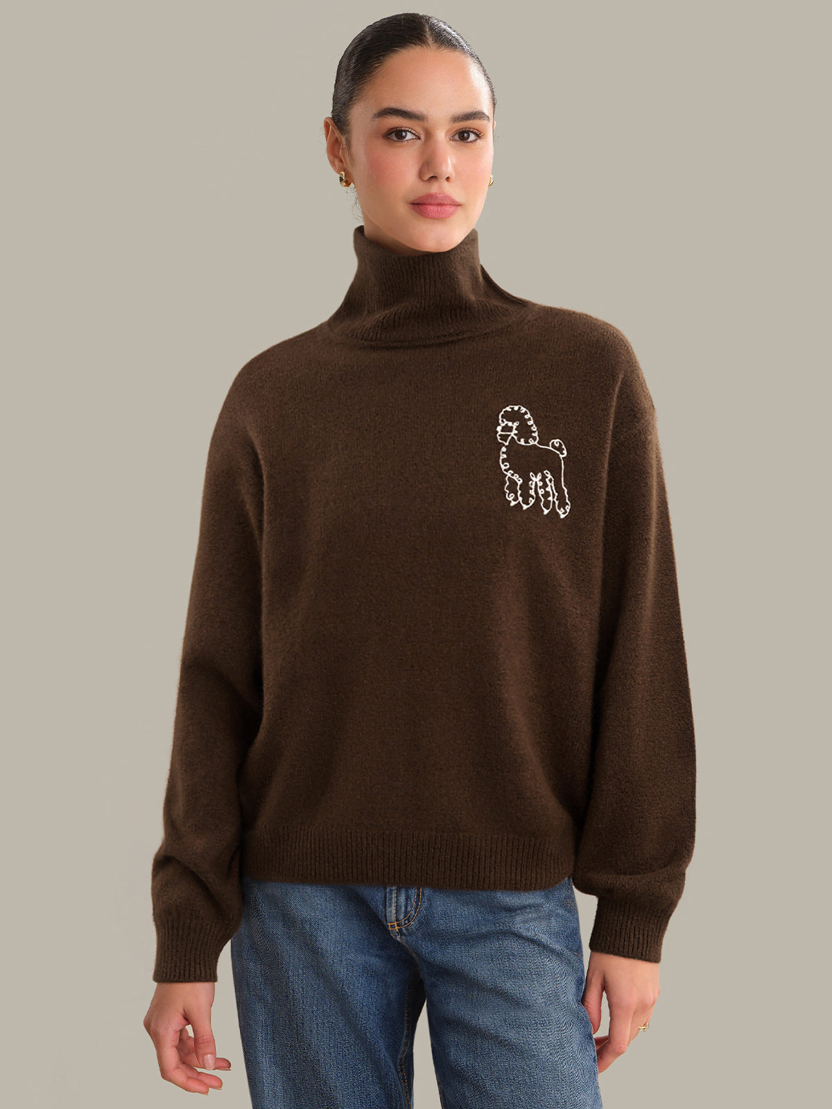 Person wearing a brown turtleneck sweater with a logo on a plain background