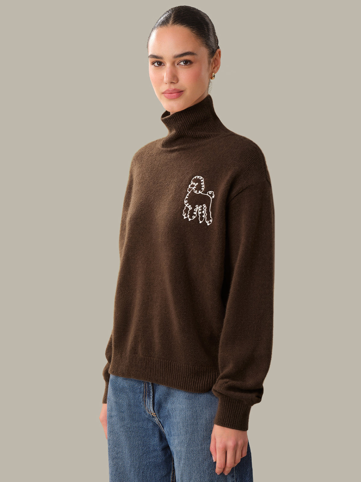 Woman wearing a brown turtleneck sweater with a white logo on a gray background