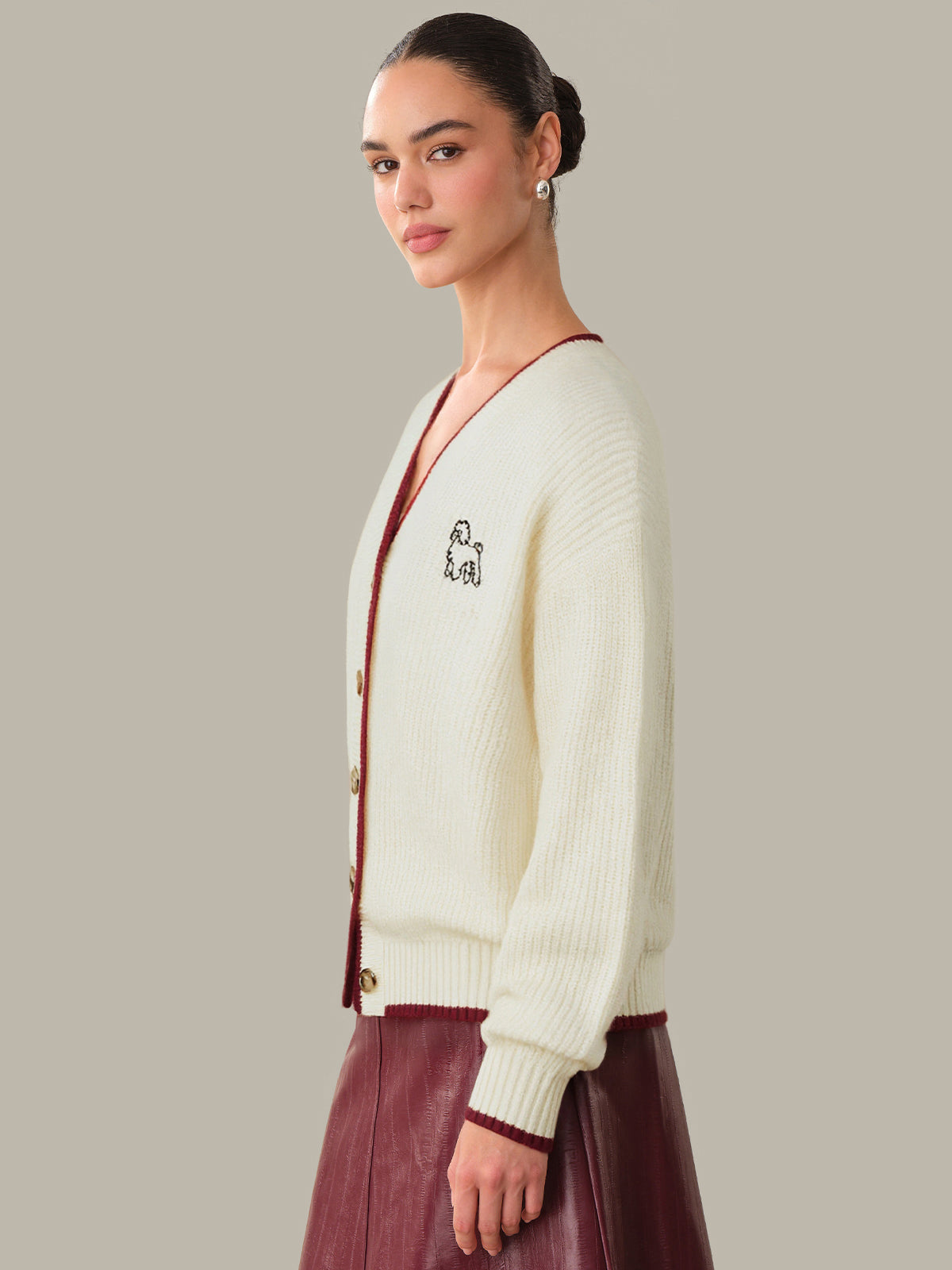 Woman wearing a cream cardigan with a logo on a plain background