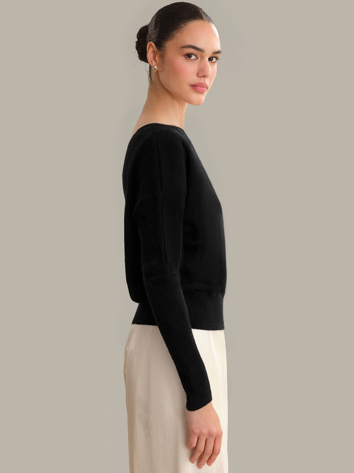 Woman wearing a black sweater and beige pants against a gray background