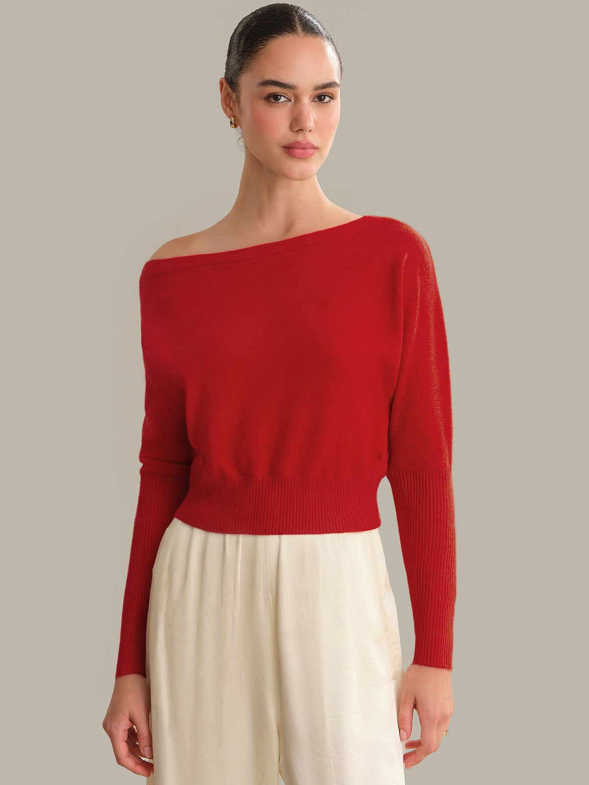 Woman wearing a red one-shoulder sweater against a neutral background