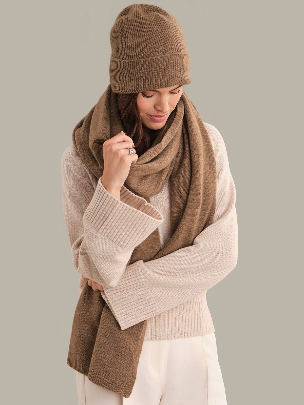 Woman wearing a brown knit hat and scarf against a plain background