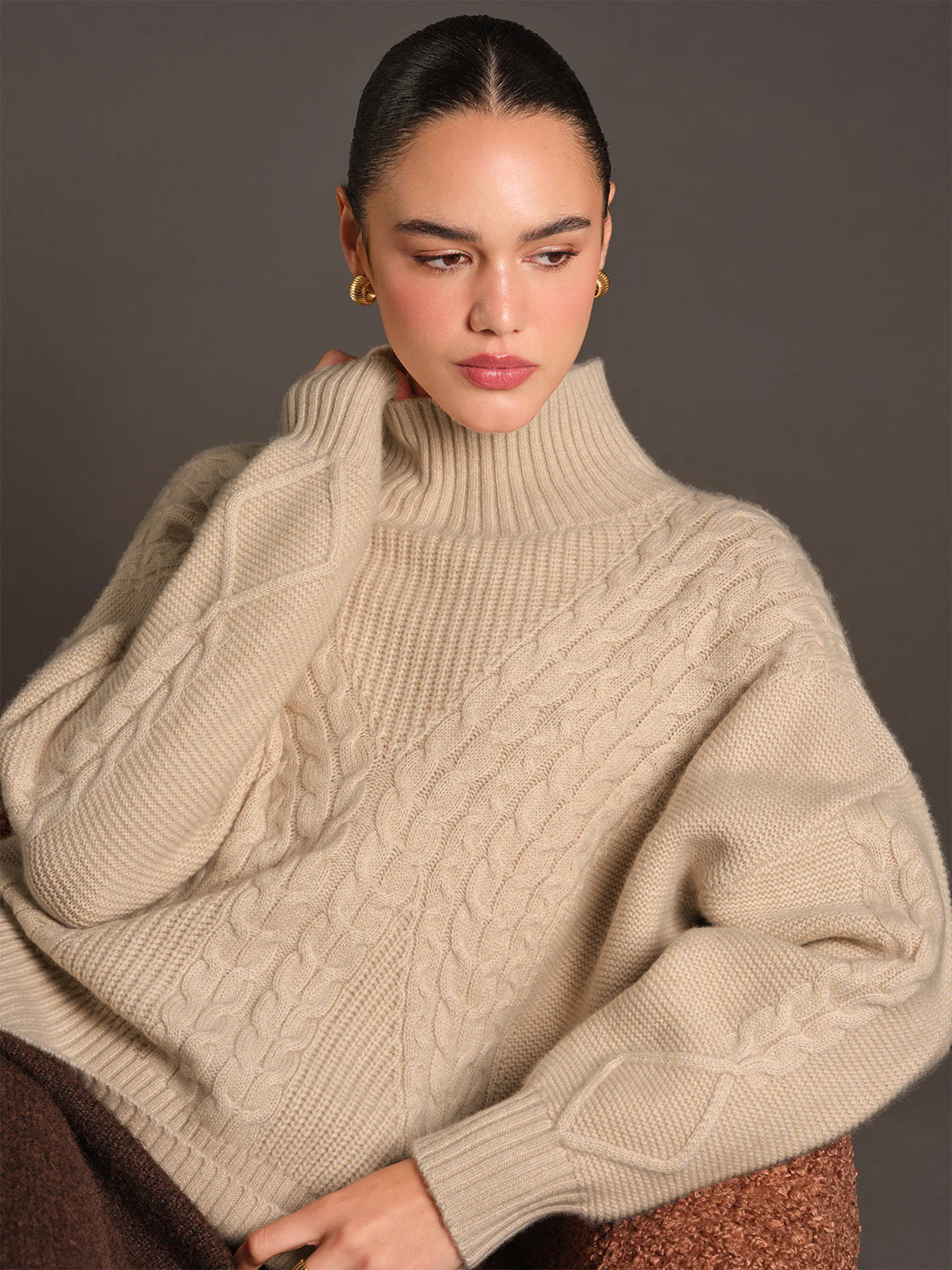 Woman wearing a beige cable knit sweater against a plain background