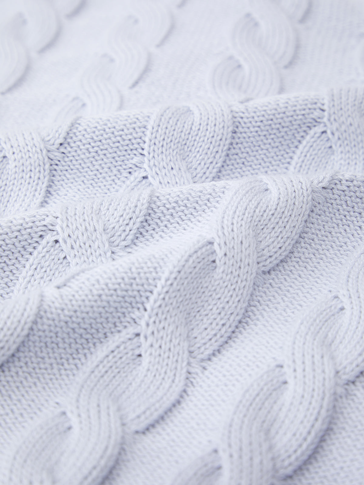 A close-up of a light-colored cable knit fabric resembles a cozy Cable Cardigan by 525 America. The patterns interlocking loops capture warmth and seasonal colors, showcasing intricate knitting details that exude comforting charm.