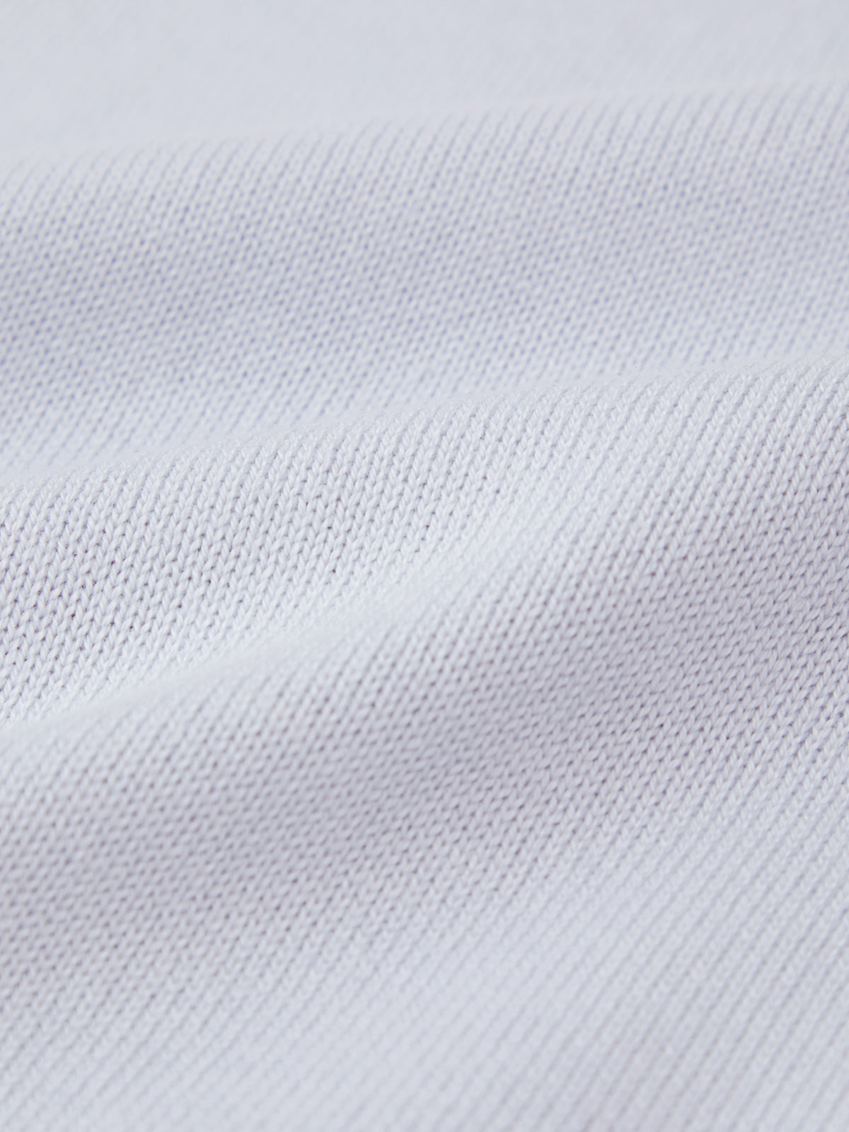 This close-up of 525 Americas textured white fabric shows a clear weave pattern on 100% cotton, appearing soft and smooth. Light casts gentle shadows, highlighting its texture similar to a detailed surface of a fitted silhouette.