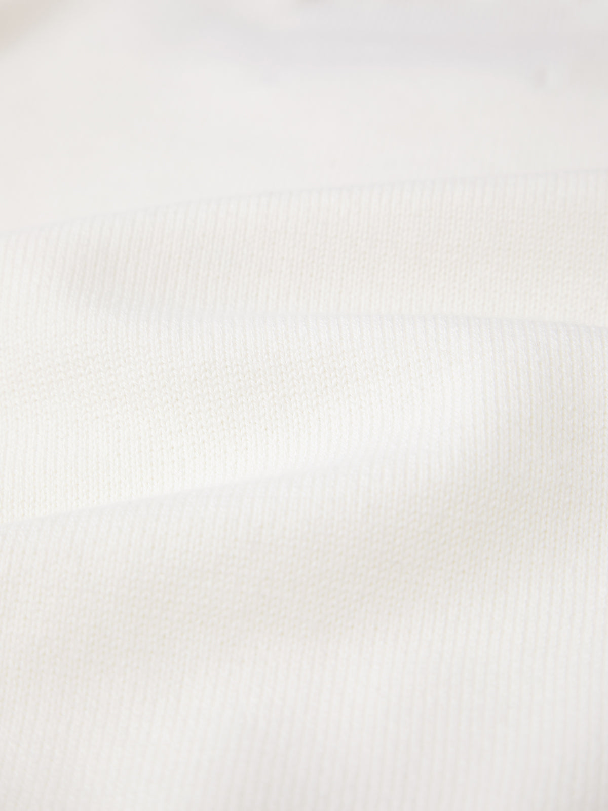 Close-up of a 525 America 100% cotton fabric with a ribbed texture and slight undulations, appearing soft and light. Shadows emphasize the gentle folds and knit pattern reminiscent of a cozy feminine pullover.