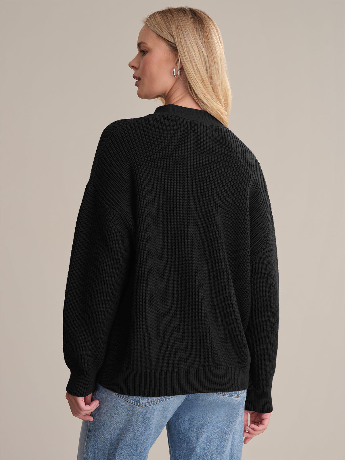 Wearing a 525 America black ribbed sweater—ideal for layering—and light blue jeans, a person with long blonde hair stands with their back turned and head slightly to the side against a neutral background.
