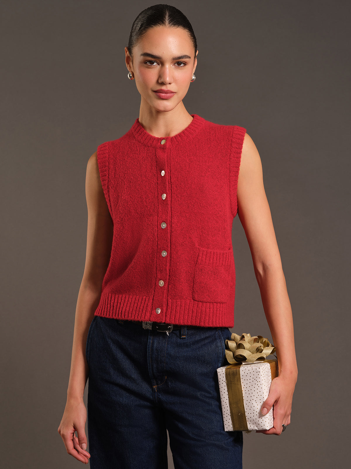 Woman wearing a red knitted vest holding a gift box against a gray background